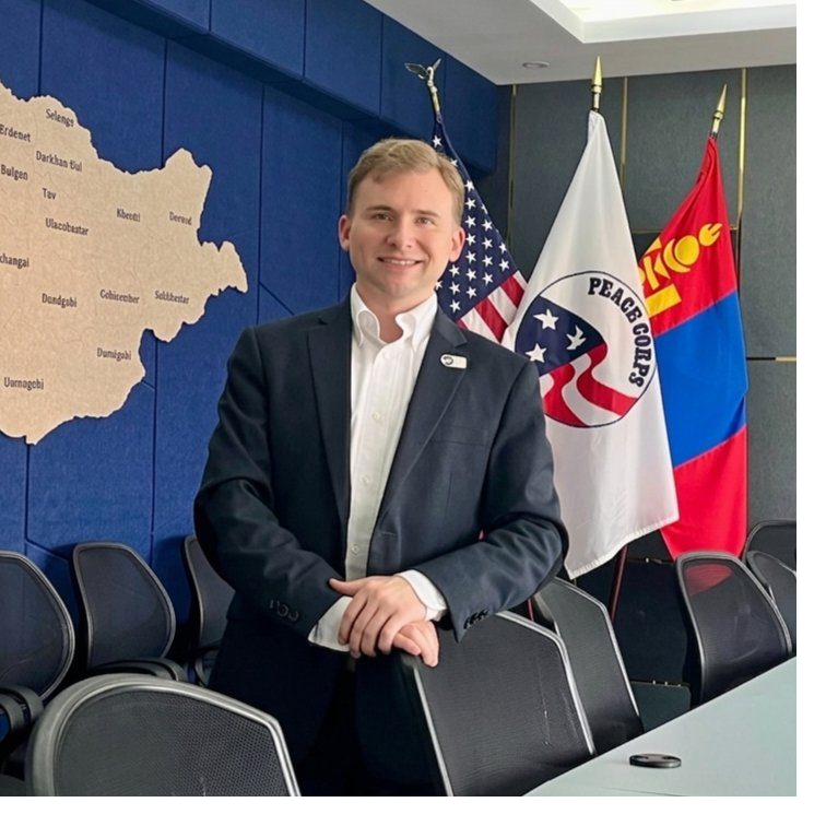 Christopher Wizda with the United States, Peace Corps, and Mongolia flags and a map of Mongolia